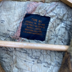 May include: Close-up of a vintage jacket lining. The lining features a map design with red and white striped accents. A navy blue tag displays text including "TYPE G-1" and "U.S. ARMY AIR FORCES".