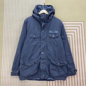 May include: A blue hooded jacket with multiple front pockets and button closures. The jacket features the "AVIREX" logo on the chest and a buttoned cuff detail. The jacket is made of a durable material.