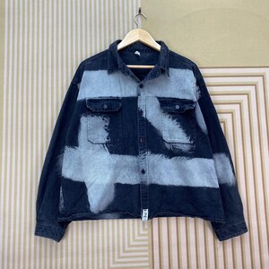 May include: A dark denim shirt with a distinctive light grey cross-patterned design. The long-sleeved shirt has two chest pockets and a button-down front. The shirt is suspended from a wooden hanger.