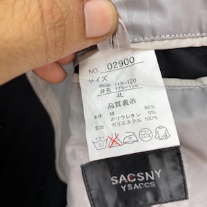 Puede incluir: Primer plano de una etiqueta de prenda Sacsny Ysaccs. La etiqueta muestra texto japon&eacute;s con informaci&oacute;n sobre la talla y la composici&oacute;n del material. Tambi&eacute;n incluye instrucciones de lavado y el n&uacute;mero 02900.