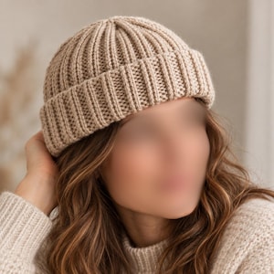 May include: A beige knit beanie with a thick, folded cuff and a vertical ribbed texture. The hat is constructed with a consistent knit pattern throughout, featuring a rounded crown and a snug fit that covers the top of the head.