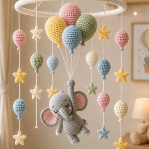 May include: A handmade crochet baby mobile featuring a gray elephant suspended by colorful balloons. The mobile includes pastel-colored balloons in pink, yellow, blue, and green, along with star-shaped accents. The mobile is designed for a nursery.
