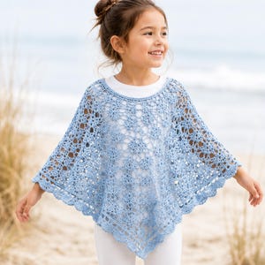 May include: A light blue crochet poncho with a floral pattern and scalloped edges. The open weave design is visible, and the poncho is worn over a white top. The garment is lightweight and suitable for warmer weather.