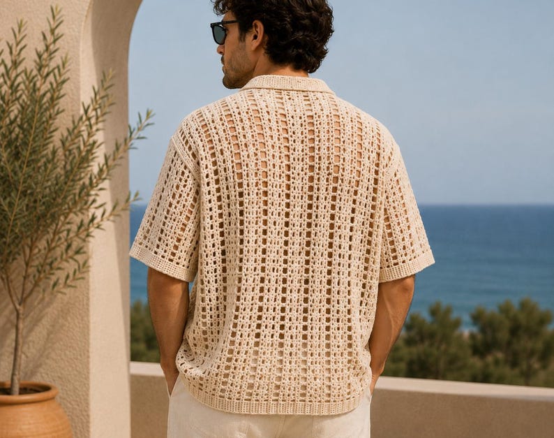 May include: A short-sleeved, open-weave shirt in a light beige color. The shirt has a collared neckline and a loose, breathable design. The image shows the back of the shirt, with the ocean visible in the background.