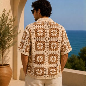 K&ouml;nnte beinhalten: Ein kurz&auml;rmeliges H&auml;kelhemd in einem quadratischen Muster aus Creme und Braun. Das Hemd hat einen Kragen und wird mit hellen Hosen getragen. Der Hintergrund zeigt das Meer und eine Topfpflanze.