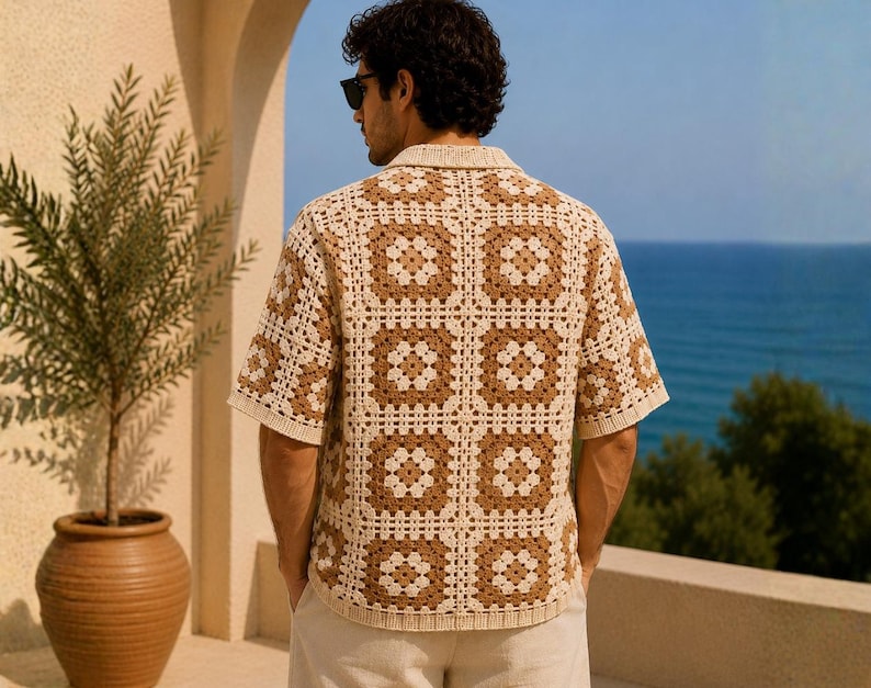 K&ouml;nnte beinhalten: Ein kurz&auml;rmeliges H&auml;kelhemd in einem quadratischen Muster aus Creme und Braun. Das Hemd hat einen Kragen und wird mit hellen Hosen getragen. Der Hintergrund zeigt das Meer und eine Topfpflanze.
