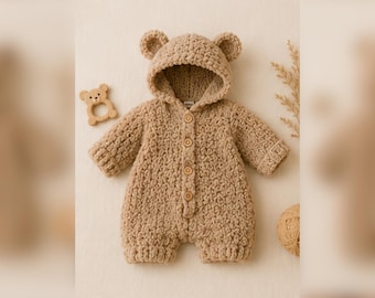 May include: A tan-colored, crocheted baby romper with a bear hood and ears. The romper has long sleeves, button closures, and short legs. A wooden bear-shaped teether is next to the romper.