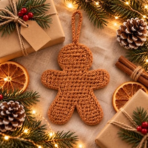 May include: A brown crocheted gingerbread man ornament with a loop at the top for hanging. The figure is crafted from yarn in a simple stitch pattern, featuring a rounded head, two arms, and two legs, designed as a flat, decorative holiday item.