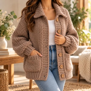 May include: A chunky knit cardigan in a solid light brown color featuring a wide collar, long sleeves with ribbed cuffs, and five round wooden buttons down the front. The garment includes two large patch pockets on the lower front section.