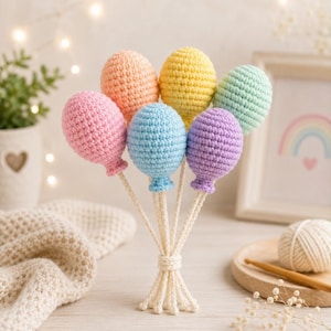 Peut inclure: Un ensemble de six ornements en crochet en forme de ballons aux tons pastel rose, pêche, jaune, bleu clair, violet et vert menthe. Chaque ballon est fixé à une fine ficelle en crochet couleur crème, toutes les ficelles étant nouées ensemble.
