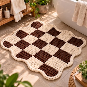 Peut inclure: Un tapis de bain rectangulaire en crochet avec un bord ondulé et festonné, présentant un motif à damier alternant des carrés de fil marron foncé et crème. Le tapis possède une surface épaisse et texturée avec une maille bouclée.