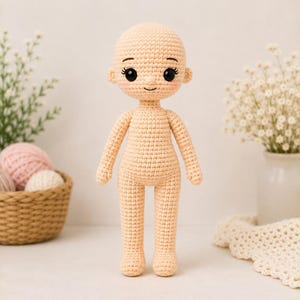 Può includere: Una bambola all'uncinetto beige con testa arrotondata, grandi occhi neri, ciglia ricamate e un piccolo sorriso. La bambola presenta un corpo con una trama a maglia uniforme in filato, color pesca chiaro con guance rosa tenue.