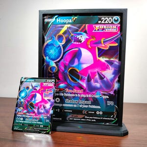May include: A standard-sized Hoopa V Fusion Strike trading card displayed next to a large, oversized jumbo version of the same card. Both cards feature the character Hoopa in a pink and purple colour scheme with 220 HP and the Shadow Impact attack.