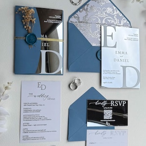 Può includere: Invito di nozze in tonalità blu e argento. Il set include inviti, biglietti di RSVP e buste, sigillati con cera. Gli inviti presentano i nomi "EMMA" e "DANIEL" a grandi lettere. Il set è decorato con elementi floreali.