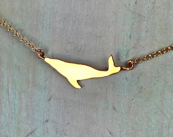 Op de afbeelding: Een gouden ketting met een walvis hanger. De walvis is een eenvoudige silhouet met een gladde, gepolijste afwerking.