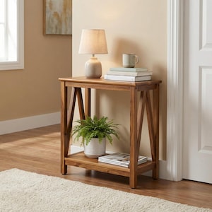 May include: A wooden console table with a lower shelf and angled legs. A small lamp with a beige shade sits on top, along with a stack of books and a mug. A potted fern and magazines are on the lower shelf.