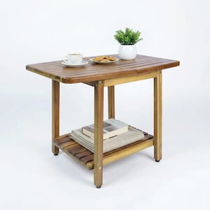 May include: A small, rectangular wooden side table with a lower shelf. The table has a natural wood finish and is topped with a white teacup and saucer, a plate of cookies, and a small potted plant. The table is approximately 24 inches long.