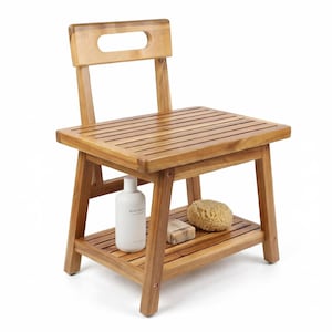 May include: Wooden shower chair with a slatted seat and backrest. The chair has a lower shelf holding a white bottle, a bar of soap, and a natural sponge. The chair is made of light brown wood.