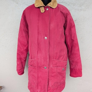May include: A long-sleeved, magenta-colored jacket featuring a tan corduroy collar, a front button-down closure with silver-toned metal buttons, and two large patch pockets on the lower front section. The jacket has a structured, heavy-duty fabric construction.