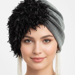 Puede incluir: Un turbante plateado y negro. El turbante est&aacute; hecho de una tela plateada brillante y tiene una secci&oacute;n de flecos negros texturizados. La mujer lleva pendientes largos de perlas.