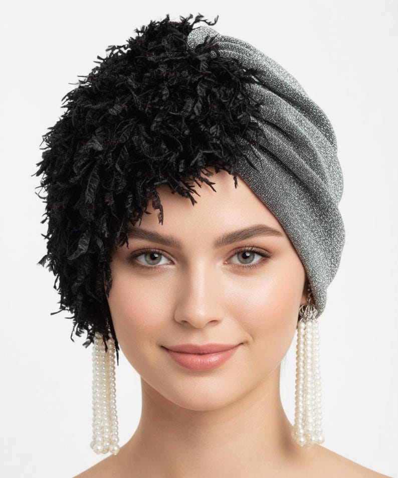 Puede incluir: Un turbante plateado y negro. El turbante est&aacute; hecho de una tela plateada brillante y tiene una secci&oacute;n de flecos negros texturizados. La mujer lleva pendientes largos de perlas.