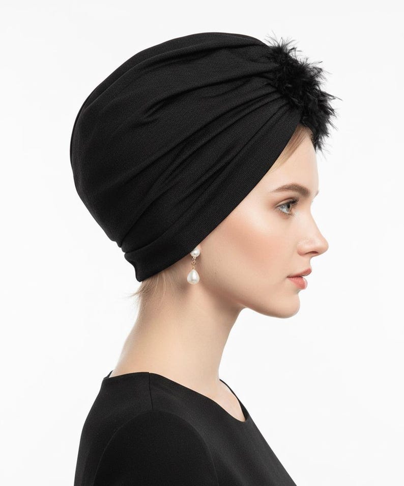 Puede incluir: Un turbante negro con un dise&ntilde;o fruncido. Un grupo de plumas negras adorna la parte superior. El tocado se usa con pendientes de perlas colgantes. El fondo es blanco.