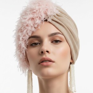 Puede incluir: Un turbante dorado con un acento de plumas rosas. El turbante se combina con pendientes largos de perlas colgantes. El tocado y las joyas crean un look glamuroso y elegante.