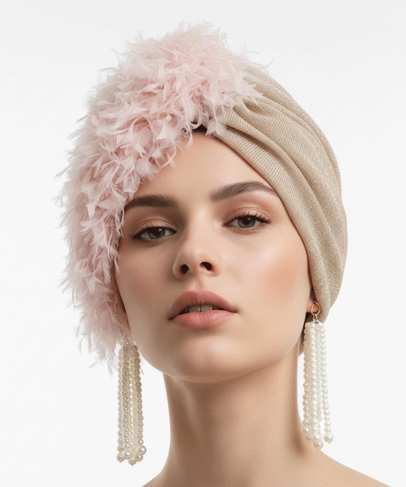 Puede incluir: Un turbante dorado con un acento de plumas rosas. El turbante se combina con pendientes largos de perlas colgantes. El tocado y las joyas crean un look glamuroso y elegante.