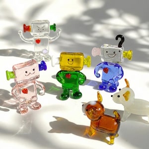 May include: A collection of colorful glass figurines, including robots and dogs. The robots are square-headed with heart-shaped details and come in various colors like pink, green, and blue. The dogs are brown and white, with yellow accents.