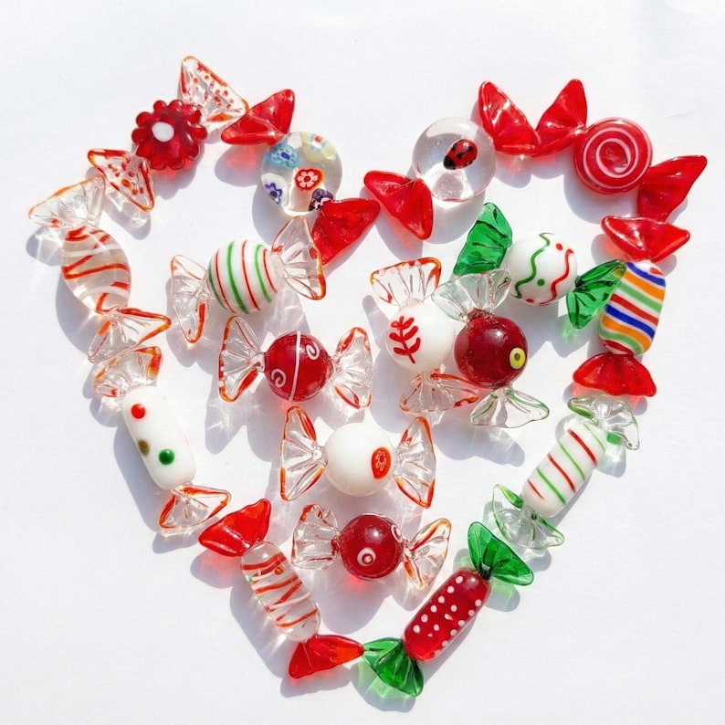 May include: A heart-shaped arrangement of colorful glass candies. The candies feature various designs, including stripes, dots, and floral patterns, with red, green, and white accents. Each piece is individually crafted, showcasing a variety of shapes and sizes.