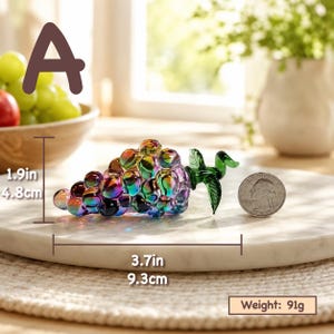 May include: An iridescent glass grape cluster figurine with a green glass leaf. The object measures 1.9 inches in height and 3.7 inches in length, with a weight of 91 grams. A US quarter coin is placed next to the glass grapes for scale.