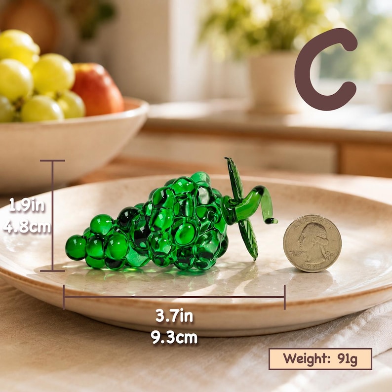 May include: A green glass grape cluster figurine with a stem and leaf detail. The object measures 1.9 inches in height and 3.7 inches in length, with a weight of 91 grams. A US quarter coin is placed next to the glass fruit for scale.
