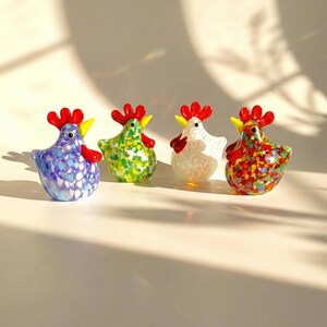 May include: Four colorful glass hen figurines. Each hen has a red comb and wattle, and a yellow beak. The hens are in shades of blue, green, white, and red with speckled patterns. Decorative figurines.
