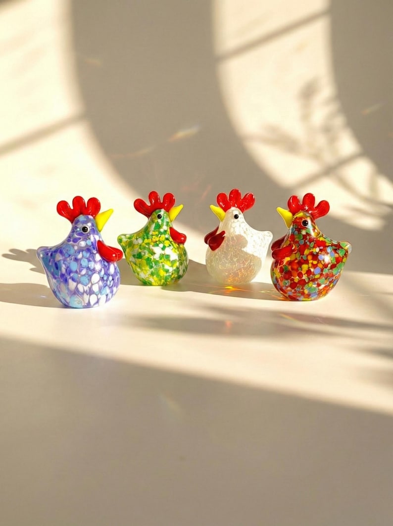 May include: Four colorful glass hen figurines. Each hen has a red comb and wattle, and a yellow beak. The hens are in shades of blue, green, white, and red with speckled patterns. Decorative figurines.