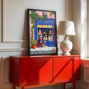 Charming Paris café art print featuring a classic blue storefront on a quaint city street, with a small dog waiting patiently beside a table of pastries. Croissants and coffee add a cozy morning feel, while soft light and European details evoke a relaxed Parisian atmosphere. Elegant yet whimsical wall art perfect for kitchens, cafés, or living spaces, celebrating travel, food, and everyday moments in France.