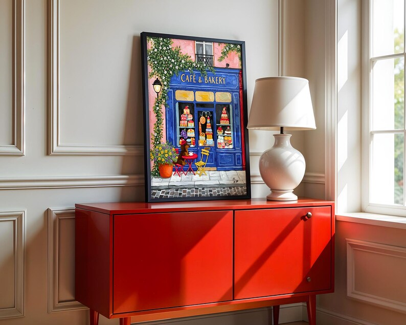 Charming Paris café art print featuring a classic blue storefront on a quaint city street, with a small dog waiting patiently beside a table of pastries. Croissants and coffee add a cozy morning feel, while soft light and European details evoke a relaxed Parisian atmosphere. Elegant yet whimsical wall art perfect for kitchens, cafés, or living spaces, celebrating travel, food, and everyday moments in France.
