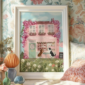 May include: A framed art print of a pink cafe called "The Dreaming Daisy" with a floral facade. Two dogs sit at a table outside. The cafe has a green door and a menu board. The artwork is set in a white frame.