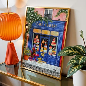 Charming Paris café art print featuring a classic blue storefront on a quaint city street, with a small dog waiting patiently beside a table of pastries. Croissants and coffee add a cozy morning feel, while soft light and European details evoke a relaxed Parisian atmosphere. Elegant yet whimsical wall art perfect for kitchens, cafés, or living spaces, celebrating travel, food, and everyday moments in France.