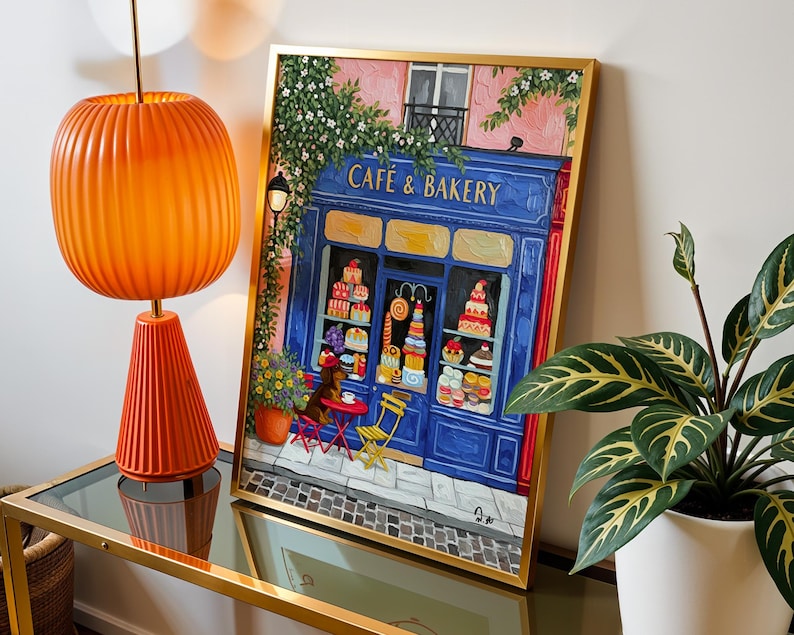 Charming Paris café art print featuring a classic blue storefront on a quaint city street, with a small dog waiting patiently beside a table of pastries. Croissants and coffee add a cozy morning feel, while soft light and European details evoke a relaxed Parisian atmosphere. Elegant yet whimsical wall art perfect for kitchens, cafés, or living spaces, celebrating travel, food, and everyday moments in France.
