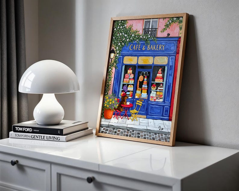 Charming Paris café art print featuring a classic blue storefront on a quaint city street, with a small dog waiting patiently beside a table of pastries. Croissants and coffee add a cozy morning feel, while soft light and European details evoke a relaxed Parisian atmosphere. Elegant yet whimsical wall art perfect for kitchens, cafés, or living spaces, celebrating travel, food, and everyday moments in France.