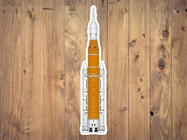 May include: A sticker featuring a detailed illustration of a rocket, primarily in orange and white. The rocket has multiple stages and is designed with intricate details, including fins and a pointed nose cone. The sticker is on a wooden background.