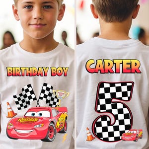 May include: White t-shirt with a colorful graphic of the character Lightning McQueen from the movie Cars, the text "BIRTHDAY BOY", checkered flags, and a trophy. The back of the shirt has the name "CARTER" and a large number "5" with a checkered pattern.