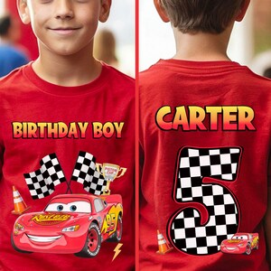 May include: Red t-shirt featuring a graphic of Lightning McQueen from the movie Cars, with the text "BIRTHDAY BOY" on the front. The back of the shirt displays the name "CARTER" and the number "5" in a checkered pattern, with a small Lightning McQueen graphic.