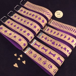 Puede incluir: Siete llaveros con tiras de corcho y tela morada. Cada llavero tiene un diseño diferente: estrellas, corazones, huesos, huellas de patas y un patrón en zigzag. Los llaveros están dispuestos en una fila, con el diseño más elaborado en la parte superior y el más simple en la parte inferior. Los llaveros están hechos con los mismos materiales y tienen un estilo similar. Los llaveros miden aproximadamente 25 cm de largo.
