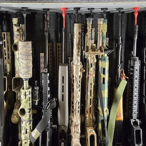 以下が含まれることがあります： さまざまなデザインと迷彩柄のライフルと銃器のコレクション。銃器は、ガンセーフに垂直に保管されています。銃器はバレル長が異なり、赤いバレルプロテクターで保護されています。