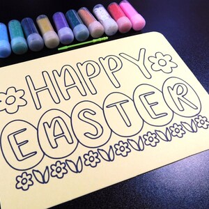 May include: A yellow cardstock craft project with the words "Happy Easter" and a row of Easter eggs outlined in blue. The cardstock is surrounded by small bottles of colourful glitter.