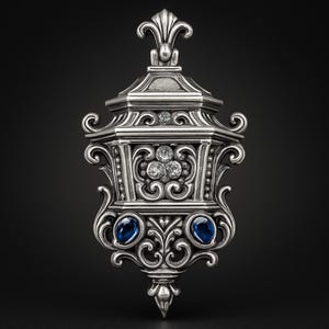 Puede incluir: Colgante de plata ornamentado con un diseño simétrico detallado. El colgante presenta un grupo central de tres piedras claras, dos piedras azules y adornos decorativos. La parte superior tiene un diseño de flor de lis.