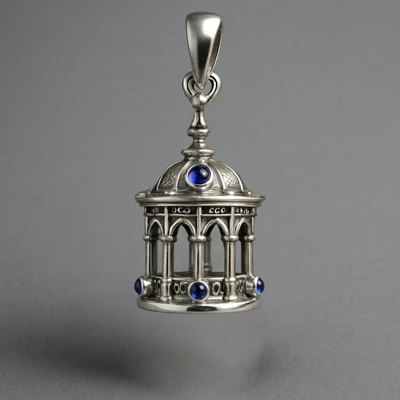 May include: Silver pendant shaped like a gazebo, with arched openings and a domed roof. It has blue gemstone accents and a loop for a chain. The pendant is a decorative item.