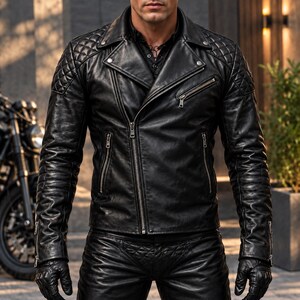 Puede incluir: Una chaqueta de moto de cuero negro con un patrón acolchado en los hombros y la parte superior de las mangas, un cuello ancho con muescas, cremalleras de metal plateado en el frente y los puños, y un cierre de cremallera principal diagonal.