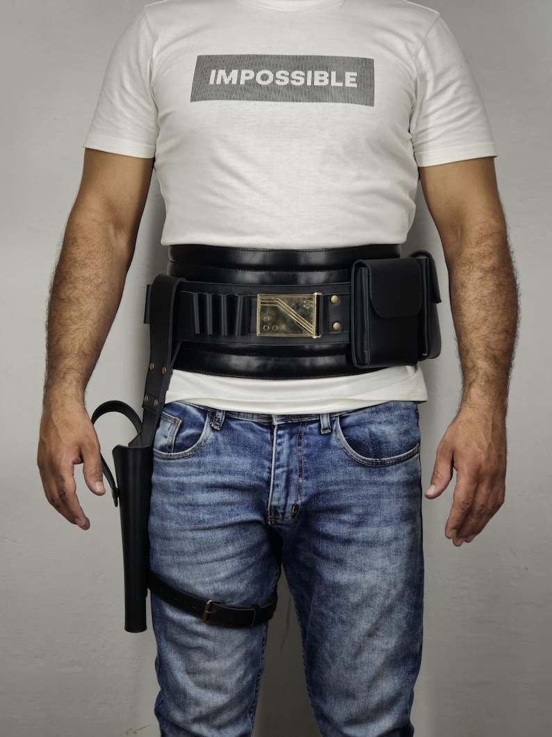 May include: A white t-shirt with the word "IMPOSSIBLE" in a black rectangle. The person is wearing a black leather belt with a holster and a pouch, and blue jeans.
